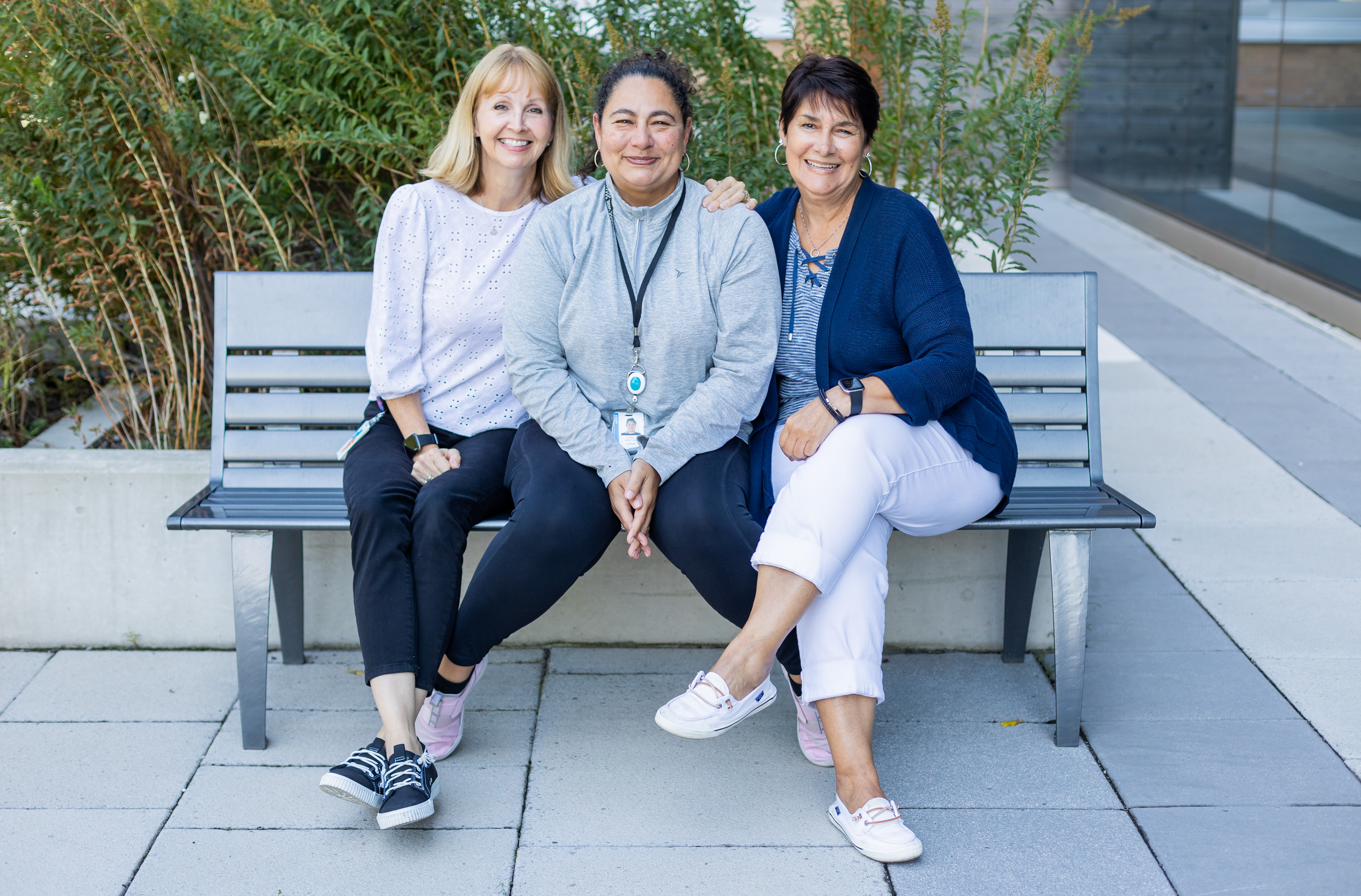 three women sitting on a bench smiling.