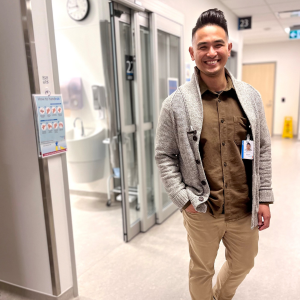 Man standing in hospital hallway smiling at camera with one hand in his pocket.