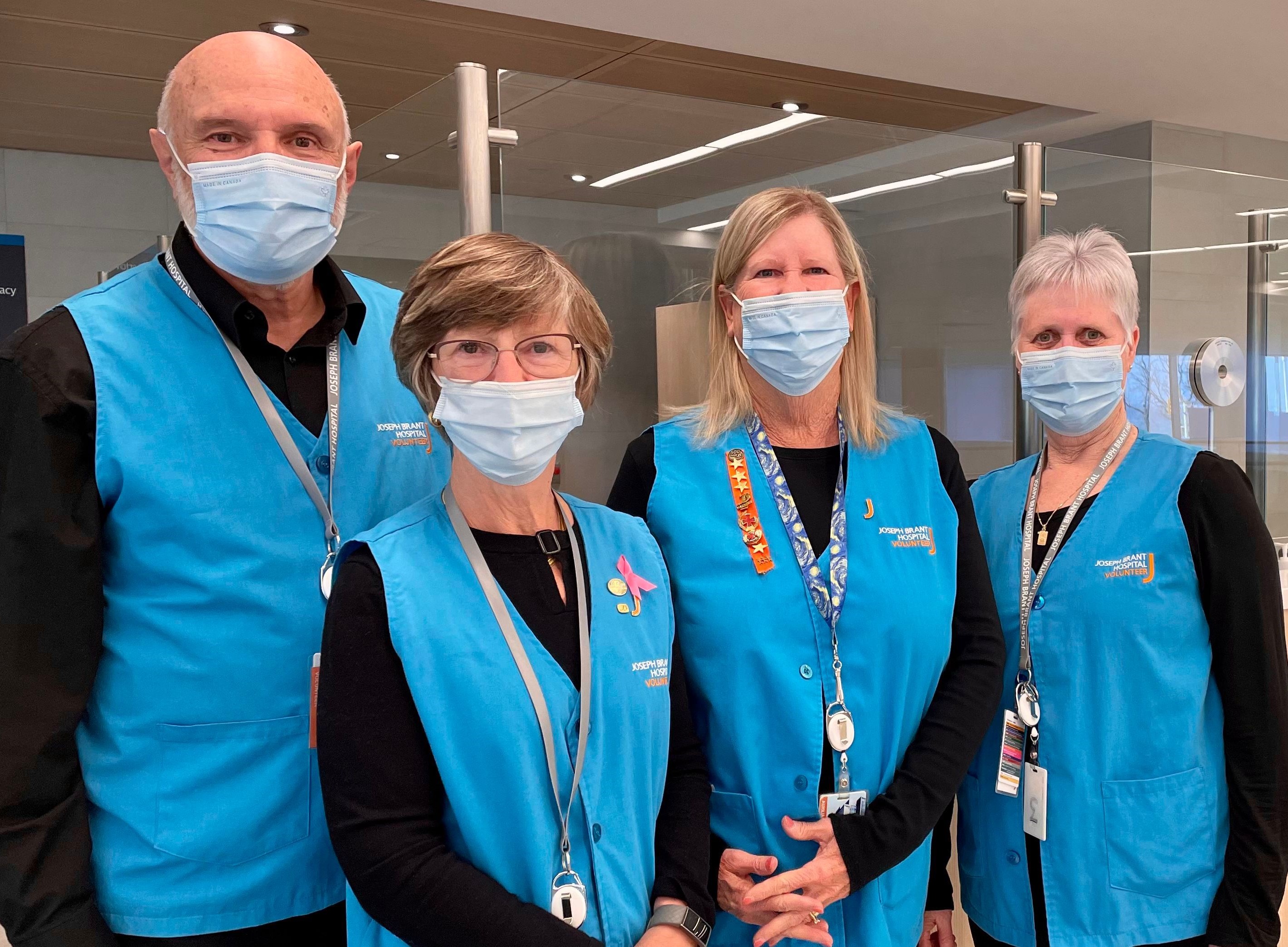 Group photo of four CARE ambassadors wearing blue volunteer vests and masks. 