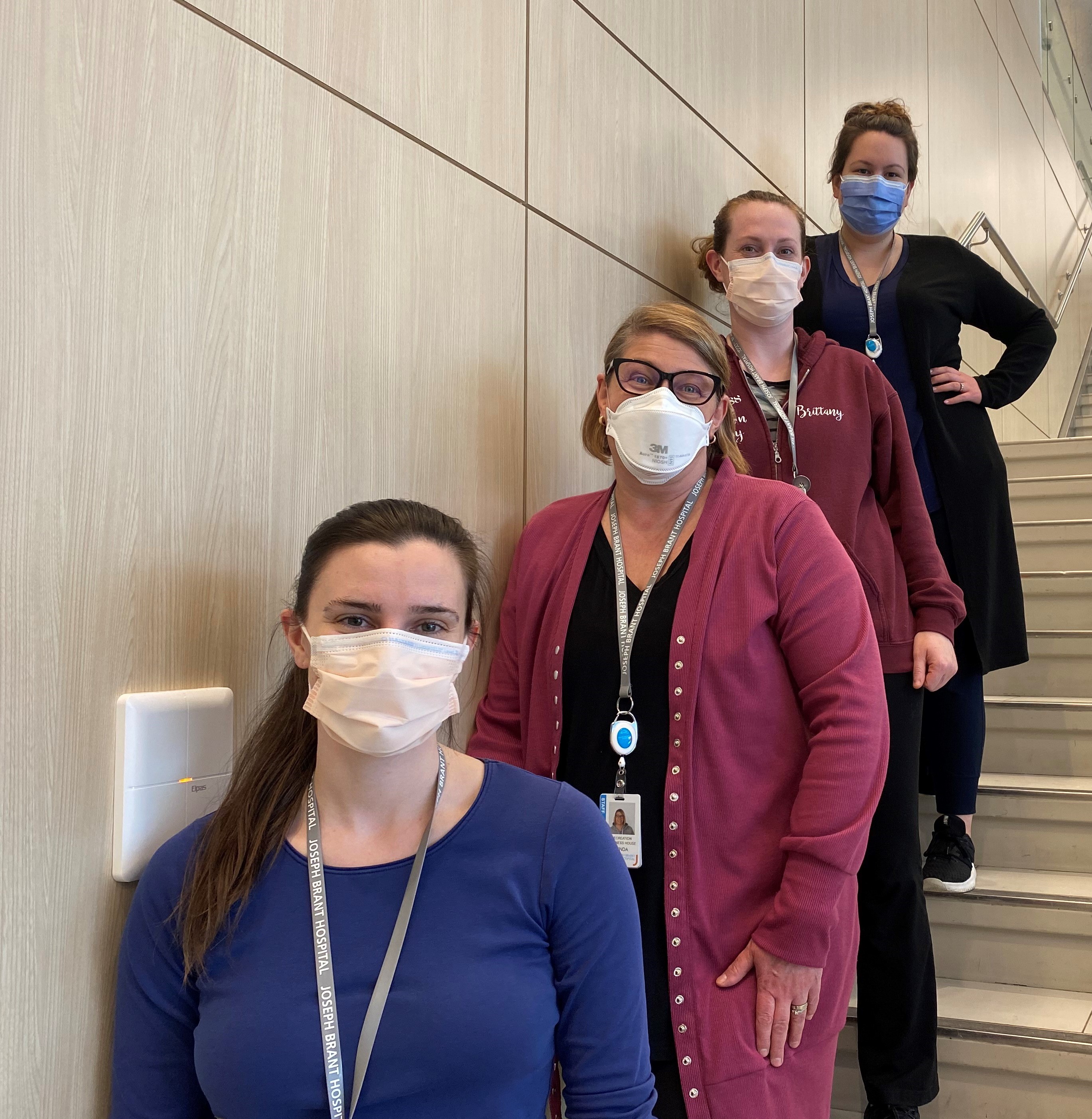 Four JBH staff wearing masks and standing behind each other on staircase. 