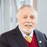 Headshot of Ted McMeekin smiling at camera from the shoulders up wearing a black blazer, red vest and tie. 
